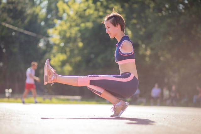 Person exercising outdoors in a balancing pose on one foot, with trees and soft sunlight in the background.