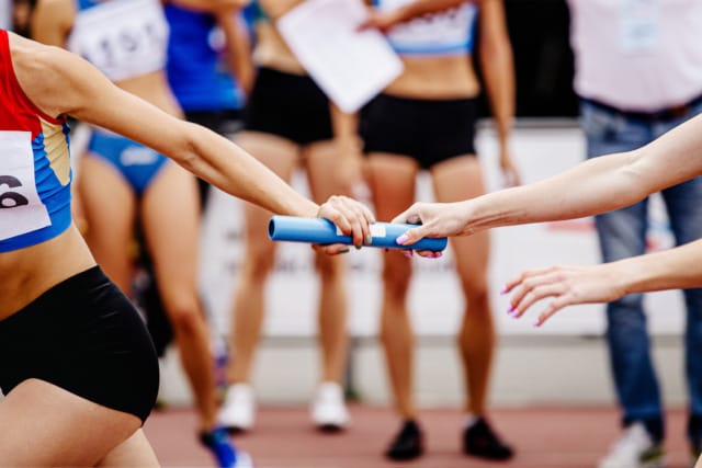Athletes in a relay race passing a baton on a track, focus on the action and vibrant sportswear.