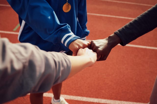 Diverse group of people doing a fist bump over a running track, symbolizing teamwork and unity.
