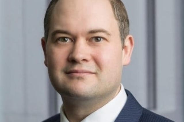Professional man in a suit and tie standing in front of a blurred background.