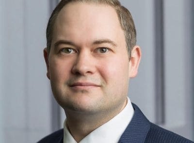 Professional man in a suit and tie standing in front of a blurred background.