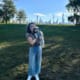 Person holding a small dog in a park with a city skyline in the background.