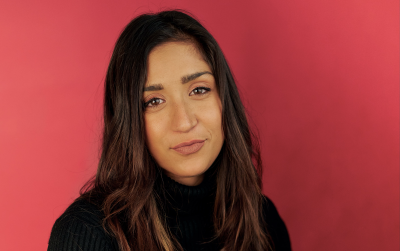 person with long hair wearing a black sweater poses against a red background