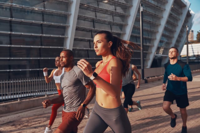 Group of diverse people jogging outdoors near a modern building on a sunny day.