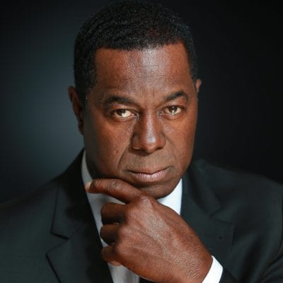 Man in a suit with a thoughtful expression, hand on chin, against a dark background