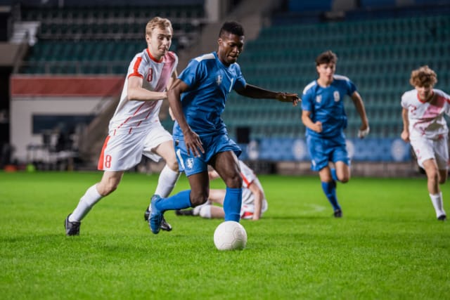 Soccer match with players in blue and white jerseys competing for the ball on a grass field.