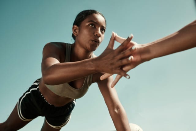 Woman in sports attire performing a high-five plank exercise outdoors on a sunny day.