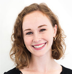 Smiling woman with curly hair wearing a black top and hoop earrings against a white background.