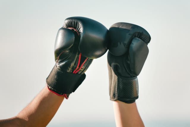 Two people wearing boxing gloves, bumping fists against a clear sky background.
