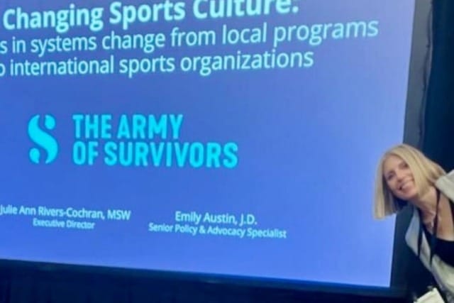 Two women smiling in front of a presentation screen about changing sports culture by The Army of Survivors.