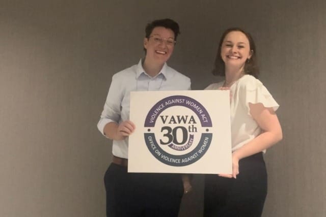 Two people smiling and holding a sign celebrating the 30th anniversary of the Violence Against Women Act.