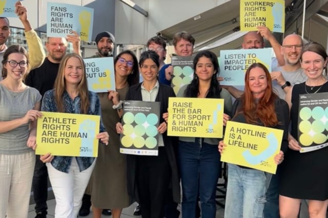 Group of people holding signs advocating for athlete and worker rights and emphasizing human rights and support hotlines.