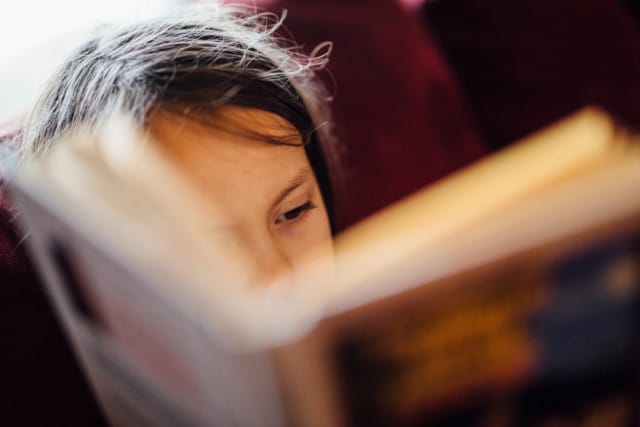 Child focused on reading a book with a blurred cover in a cozy setting
