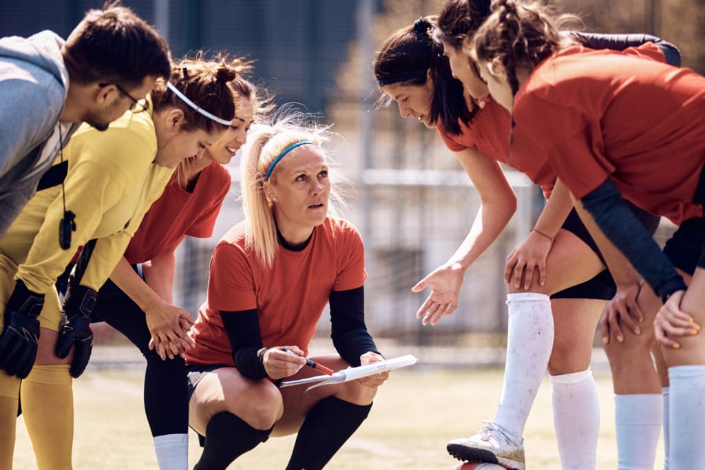 Coach discussing strategy with female soccer team players gathered on the field during a sunny day training session