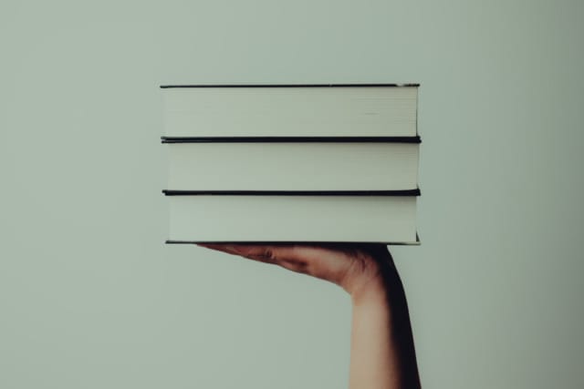 Hand holding a stack of three closed books against a plain background.