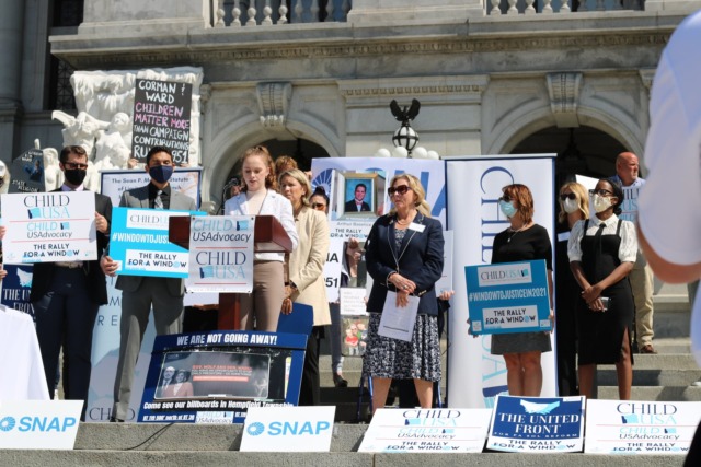 A group of people holding signs and banners at a child advocacy rally on the steps of a government building.