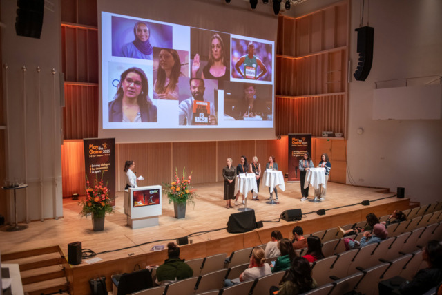 Panel discussion in a conference hall with a large screen showing diverse speakers through video calls.