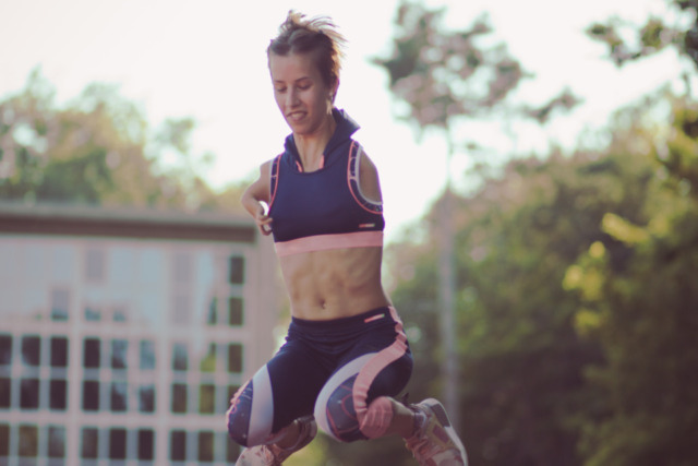Person in athletic attire mid-air while performing jump over hurdle outdoors.