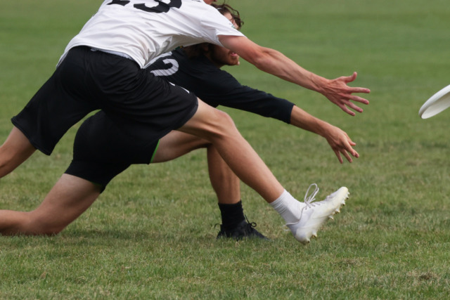 Two athletes reaching to catch a flying disc during an intense game on a grassy field.