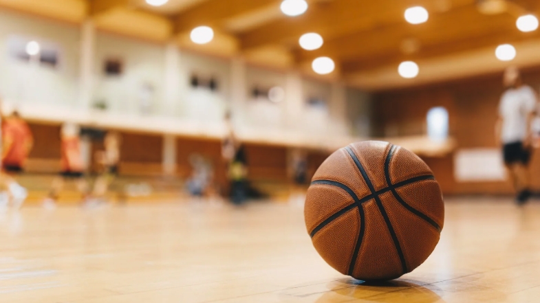 Basketball resting on an indoor court with blurred players practicing in the background.