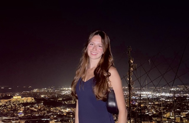 Woman smiling at night with a cityscape in the background illuminated by bright lights.