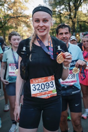 Marathon runner smiling and holding medals with other participants in the background after completing a race.