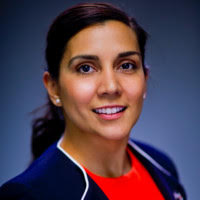 Smiling person with dark hair in a blue jacket and red top against a gradient background.