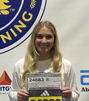 Person holding a race bib with a smile, standing in front of a backdrop with logos.