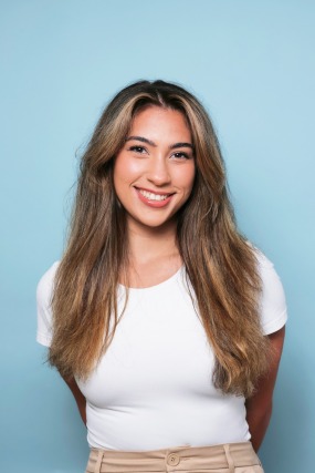 Smiling person with long hair in a white shirt against a light blue background.