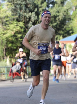 Man running a marathon wearing a beige shirt and headband, with other runners and trees in the background.
