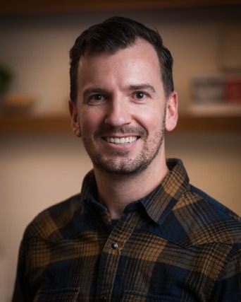 Person smiling, wearing a plaid shirt with a blurred background.
